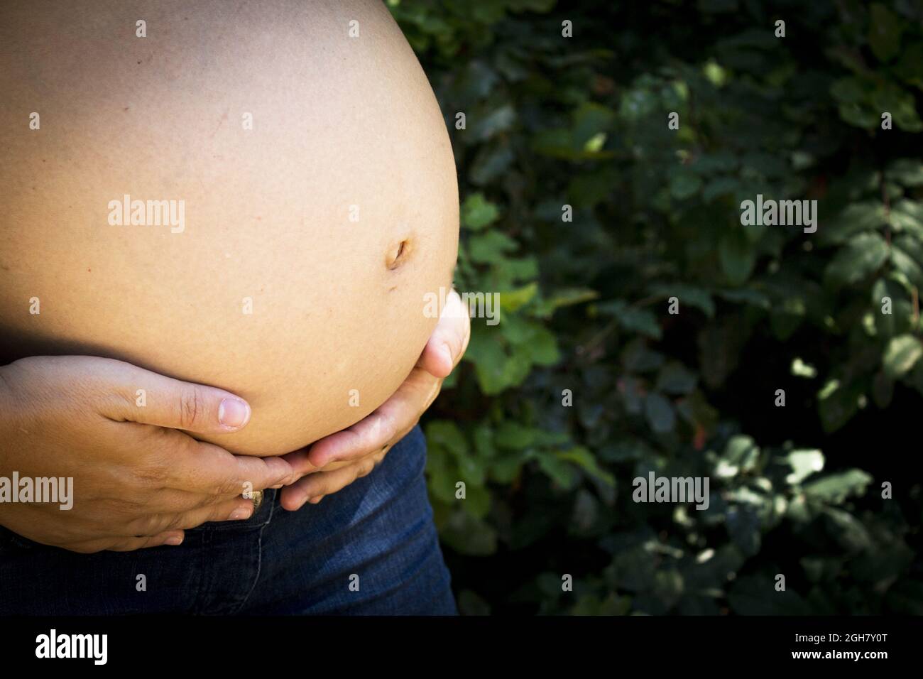 Donna incinta di sette mesi in un parco vestito di jeans Foto Stock