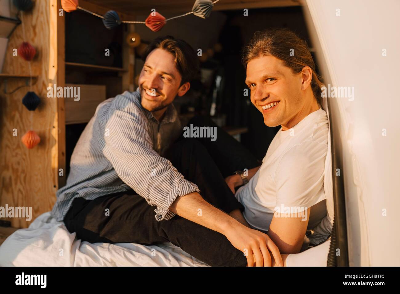 Sorridenti amici maschi che guardano via mentre si siedono in casa a motore durante il campeggio Foto Stock