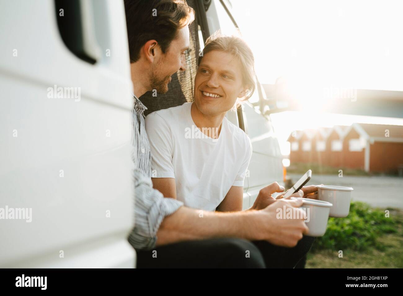 Coppia gay sorridente con una tazza di caffè che trascorre il tempo libero in un camping van il giorno di sole Foto Stock