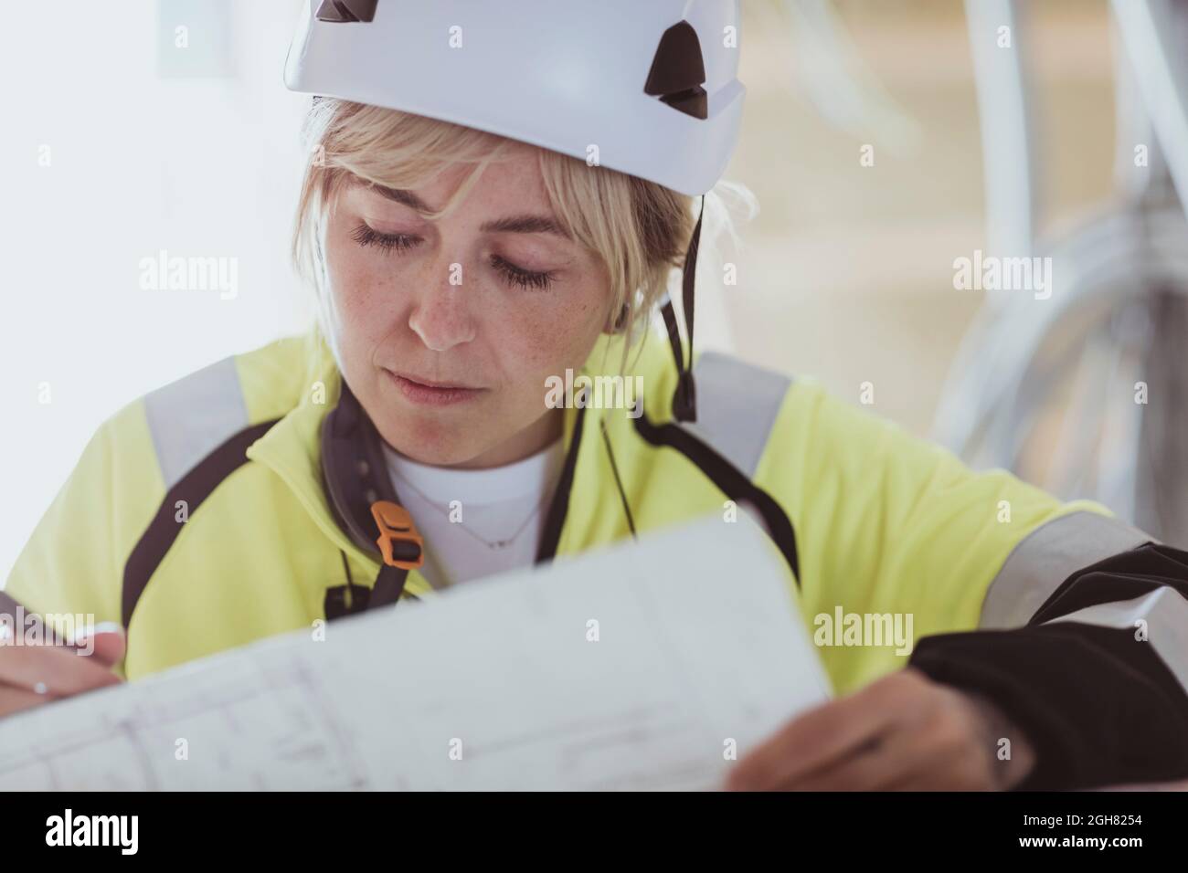 Costruttore femminile che analizza la pianta del pavimento mentre lavora in cantiere Foto Stock
