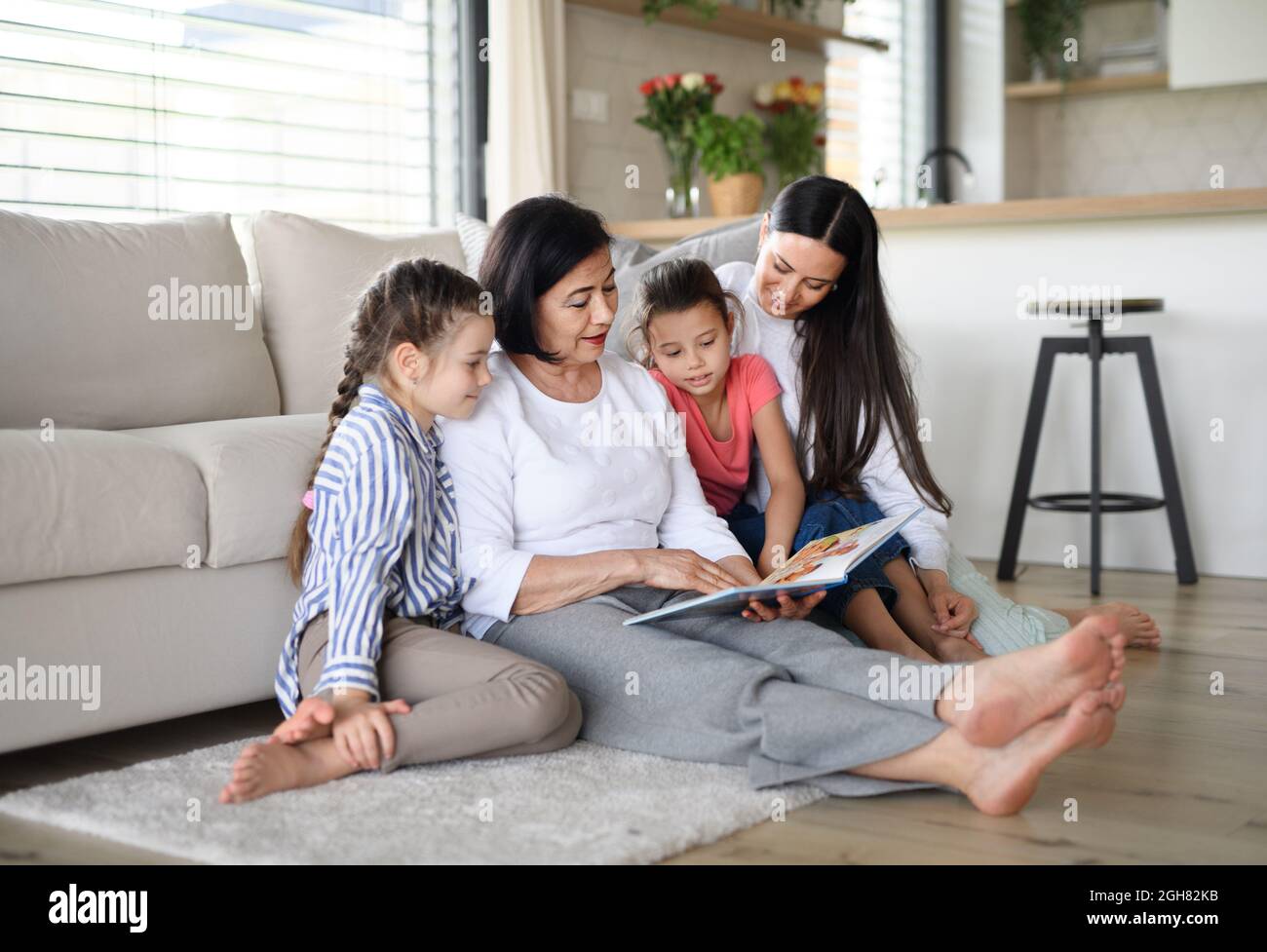 Ragazze piccole felici con la madre e la nonna all'interno a casa, libro di storia di lettura. Foto Stock