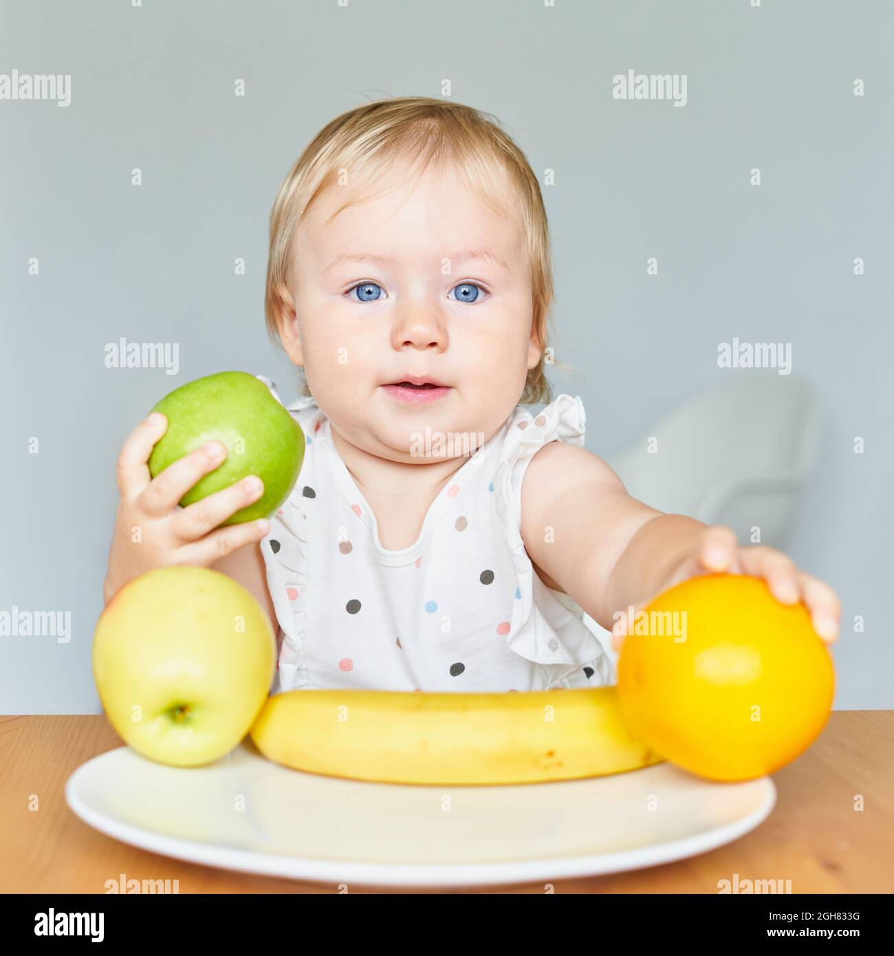 Adorabile biondo biondo biondo-eyed bambino che regge l'apla verde e l'arancione. Piatto con frutta Foto Stock