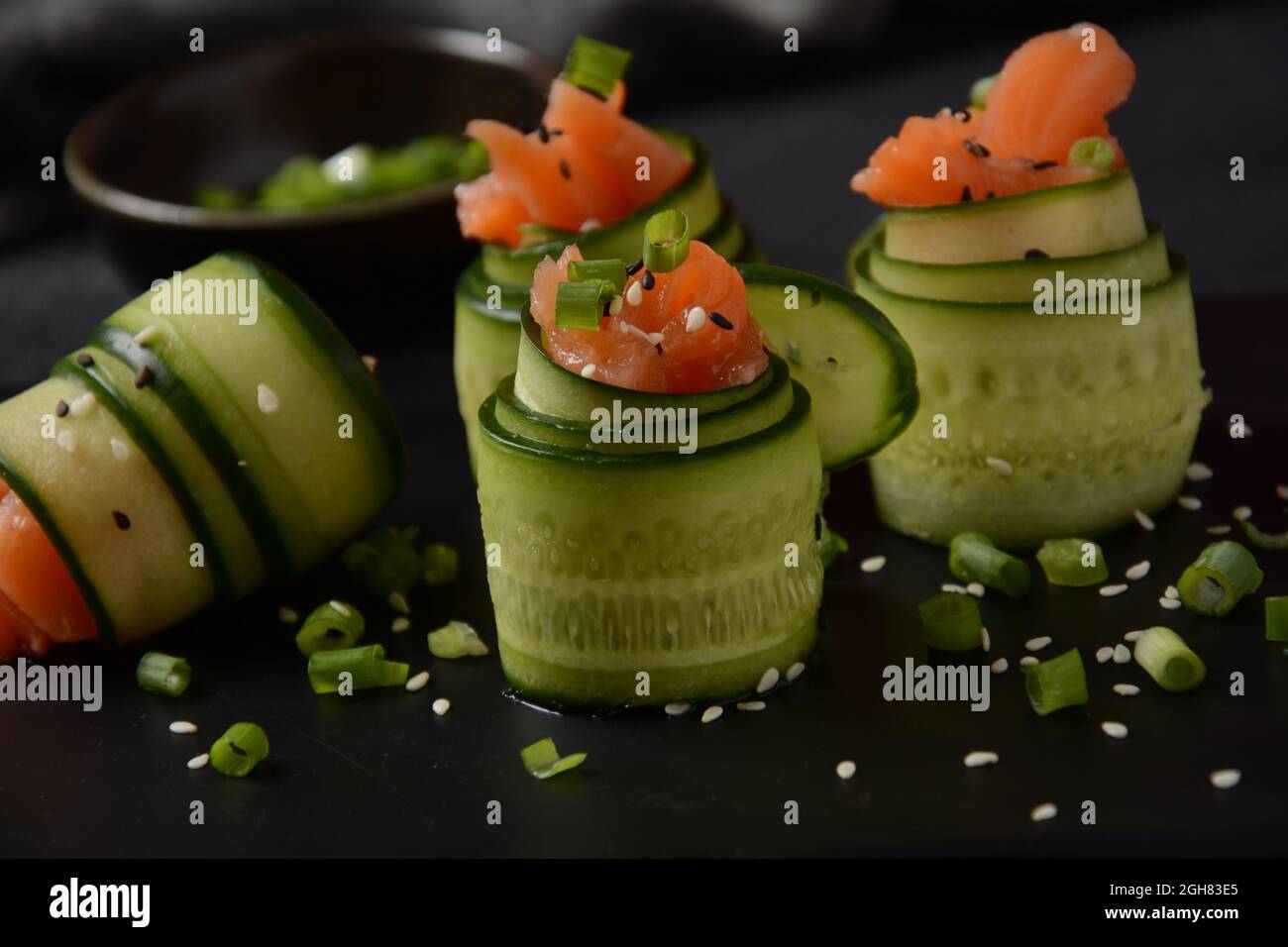 Rotoli di cetrioli con pezzi di salmone salato, semi di sesamo bianco e nero, cipolla verde tritata. Antipasti di verdure di festa Foto Stock