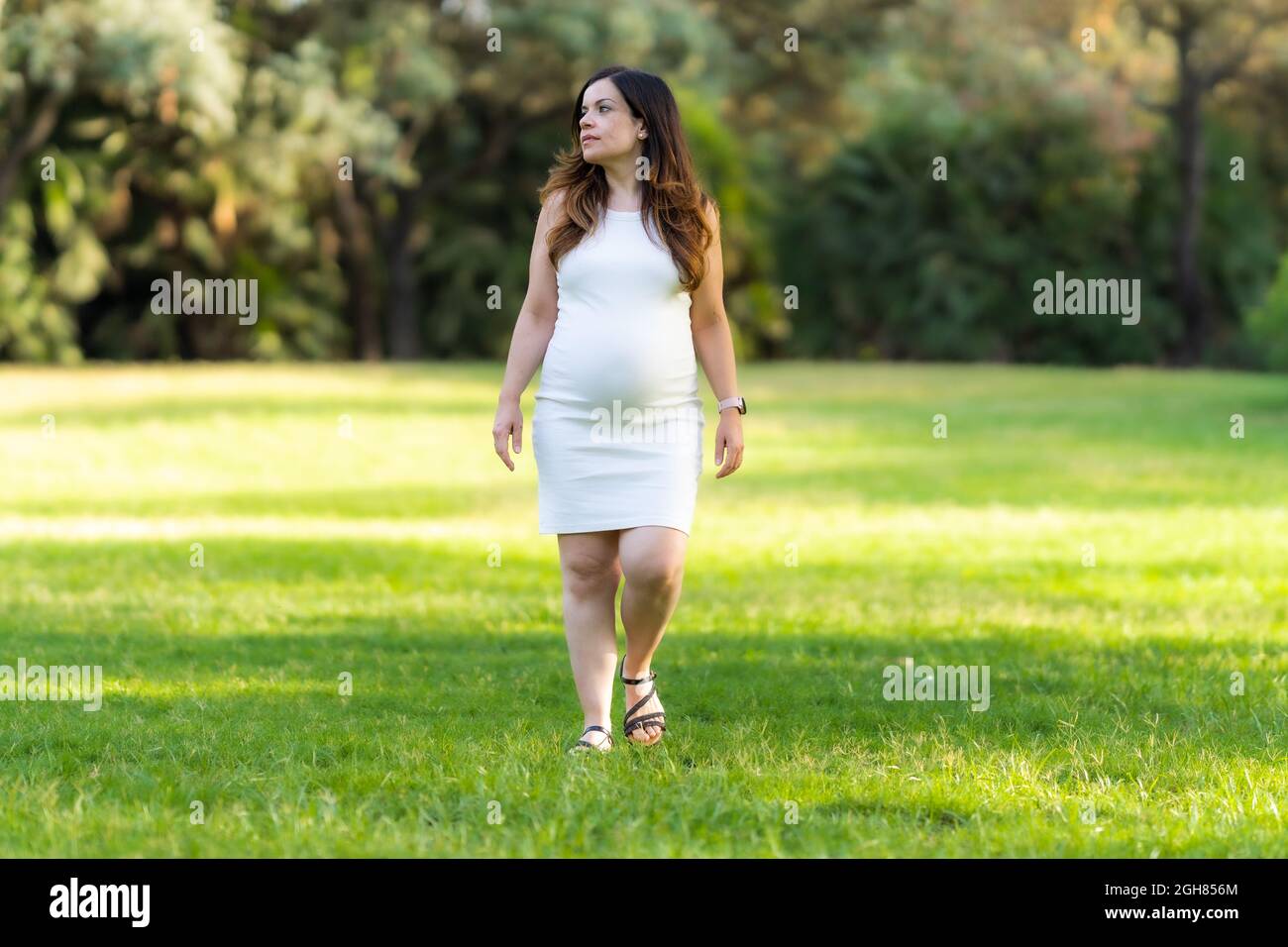 Ritratto di una donna incinta che cammina in un parco con un'espressione distratta. Foto Stock