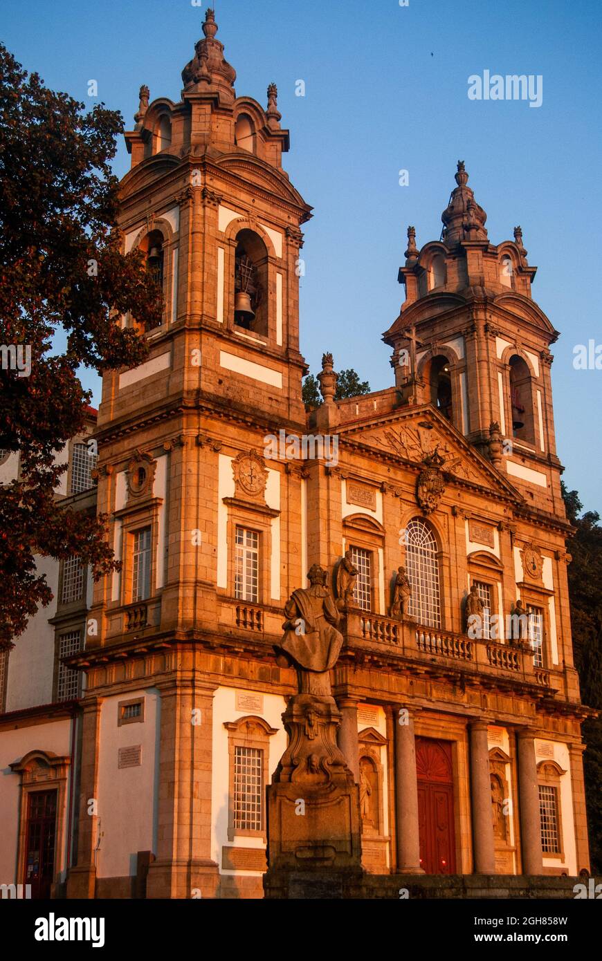 Bella chiesa in stile portoghese e una statua diventano arancioni al tramonto con un bel cielo limpido - Vertcal, Bom Jesus, Braga, Portogallo Foto Stock