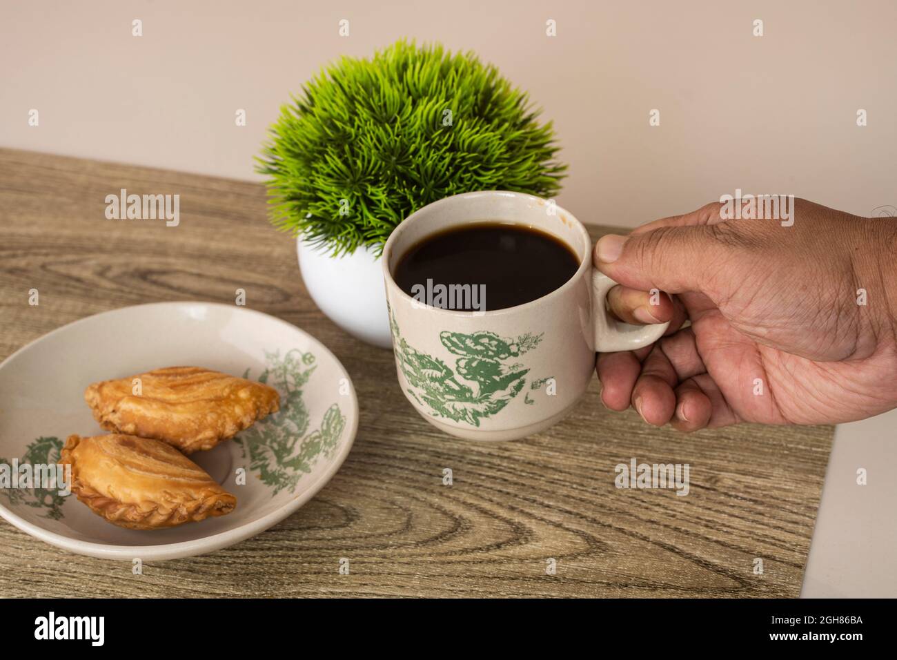 Una mano che raccoglie una tazza di caffè con la puff di curry per colazione. Foto Stock