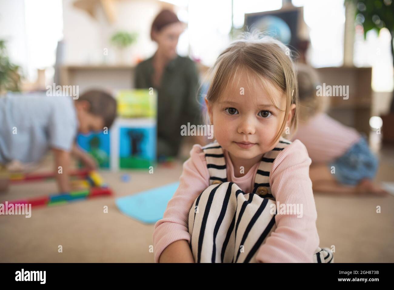 Ritratto di piccola bambina della scuola materna al chiuso in aula, guardando la macchina fotografica. Foto Stock