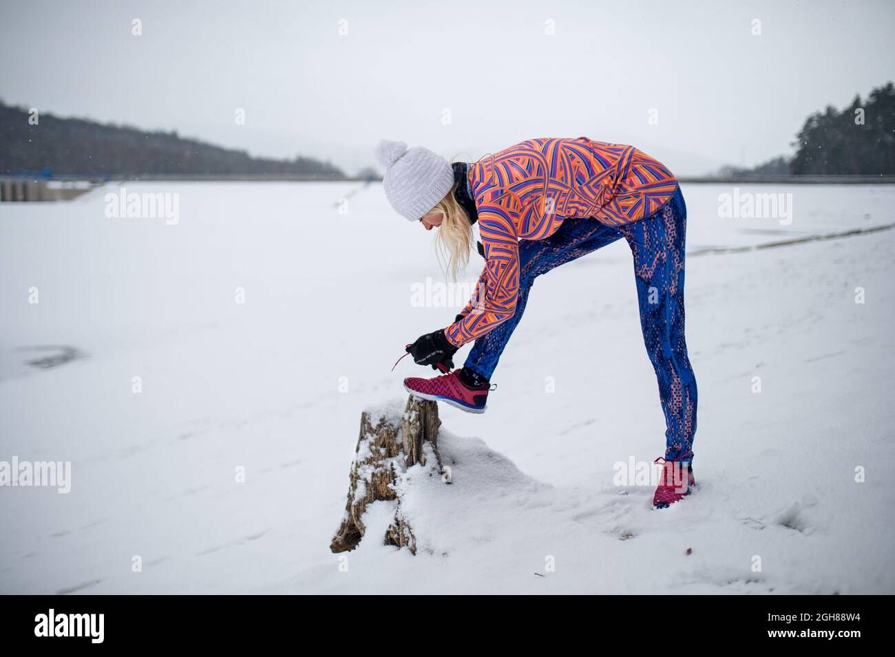 Donna anziana attiva all'aperto in inverno nevoso, allacciando scarpe. Foto Stock