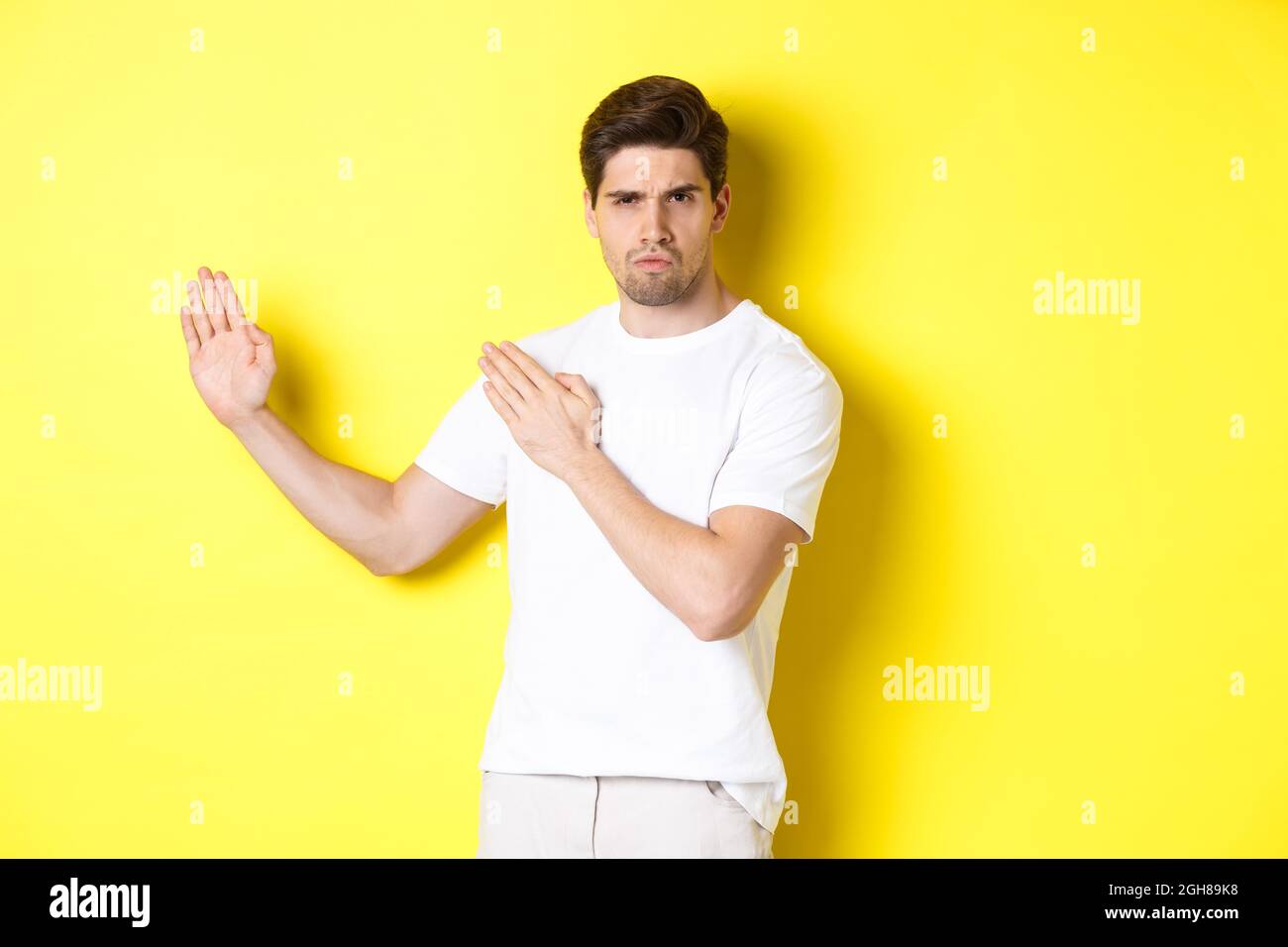 Uomo che mostra abilità kung-fu, arti marziali movimento ninja, in piedi in bianco t-shirt pronto a combattere, in piedi su sfondo giallo Foto Stock