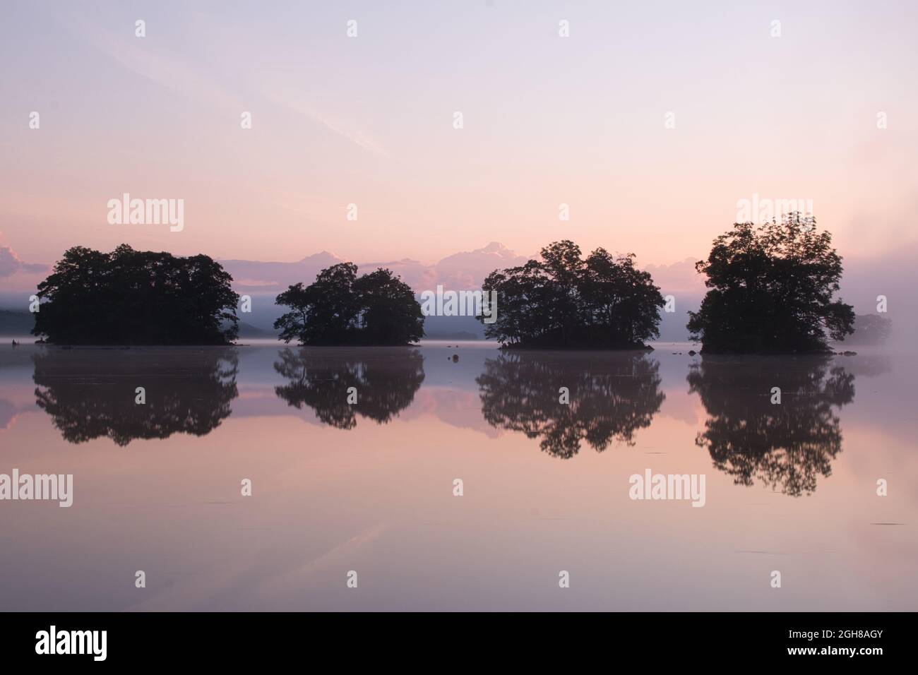 Una fila di quattro piccole isole si riflette in un lago poco prima dell'alba Foto Stock