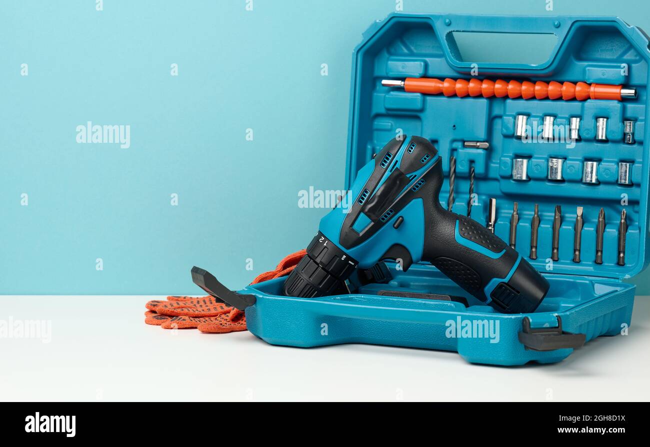 scatola in plastica con trapano a batteria e set di trapani e cacciaviti su sfondo bianco, spazio di copia Foto Stock