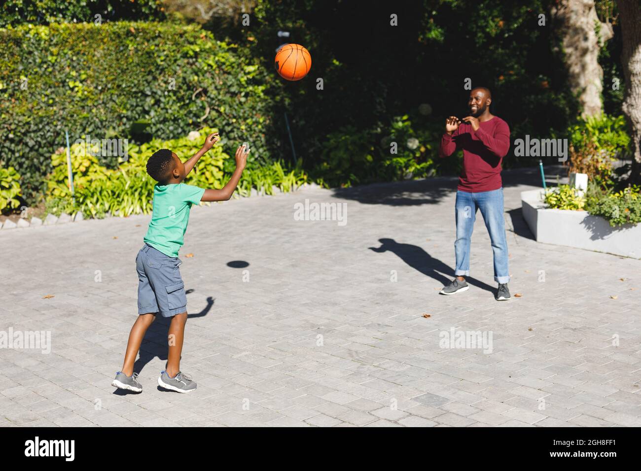 Padre afroamericano con figlio che sorride e gioca a basket in giardino Foto Stock