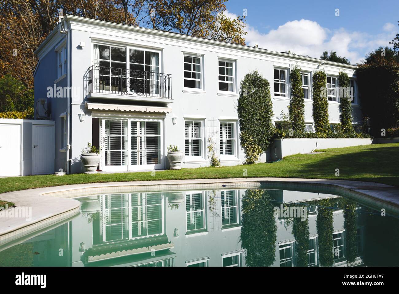 Grande casa con piscina e alberi in giardino soleggiato Foto Stock