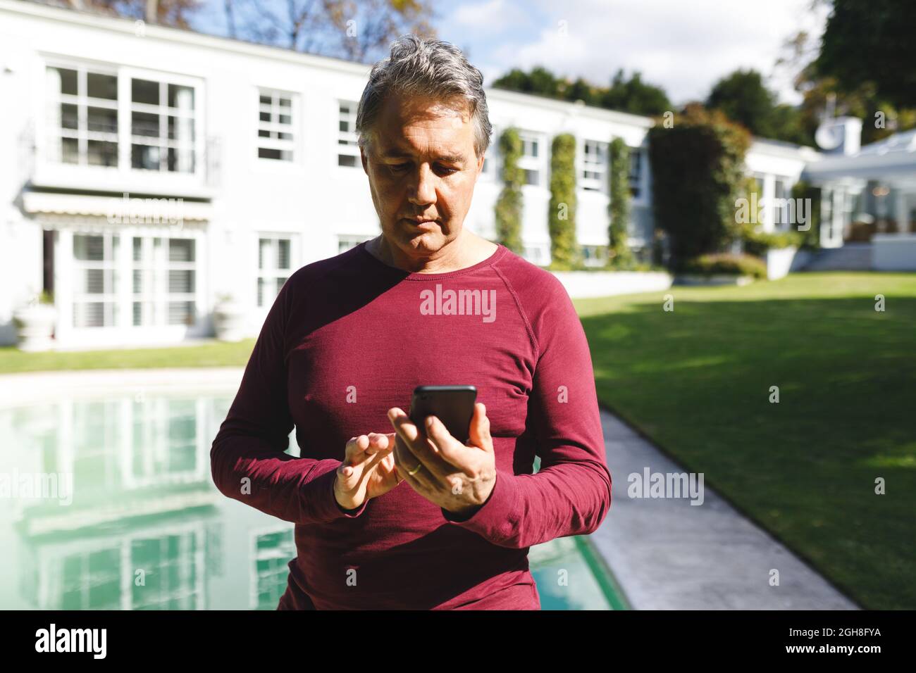 Felice uomo caucasico anziano utilizzando smartphone in giardino soleggiato Foto Stock