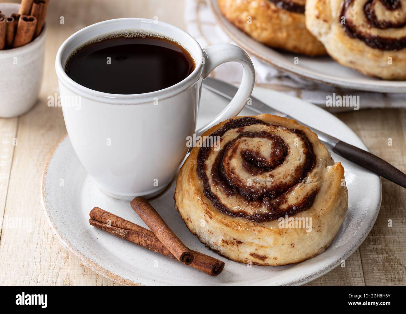Rotolo di cannella con una tazza di caffè e bastoncini di cannella su un piatto Foto Stock