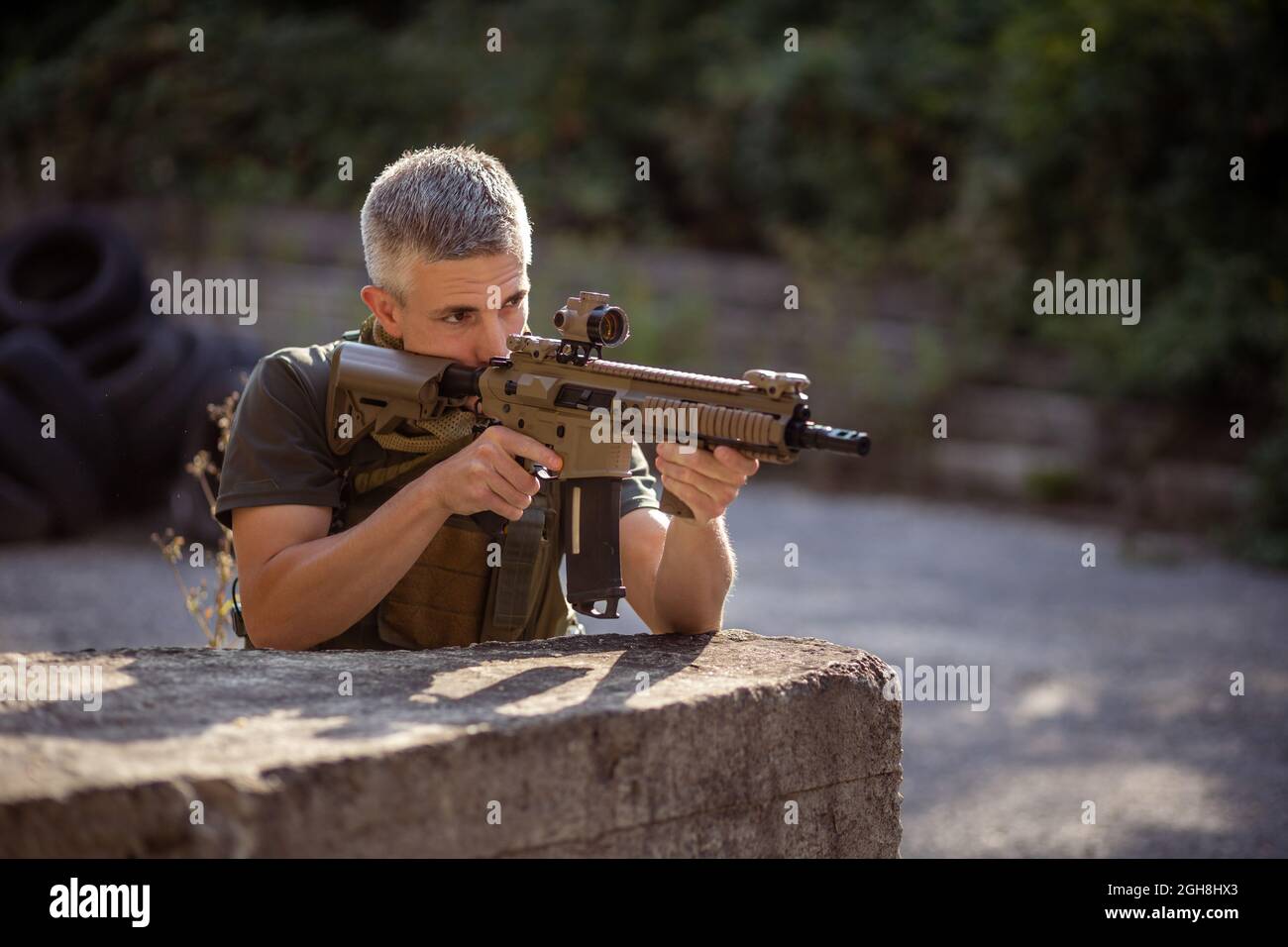 Un uomo si inginocchia dietro la cover con un fucile d'assalto airsoft in uniforme militare Foto Stock
