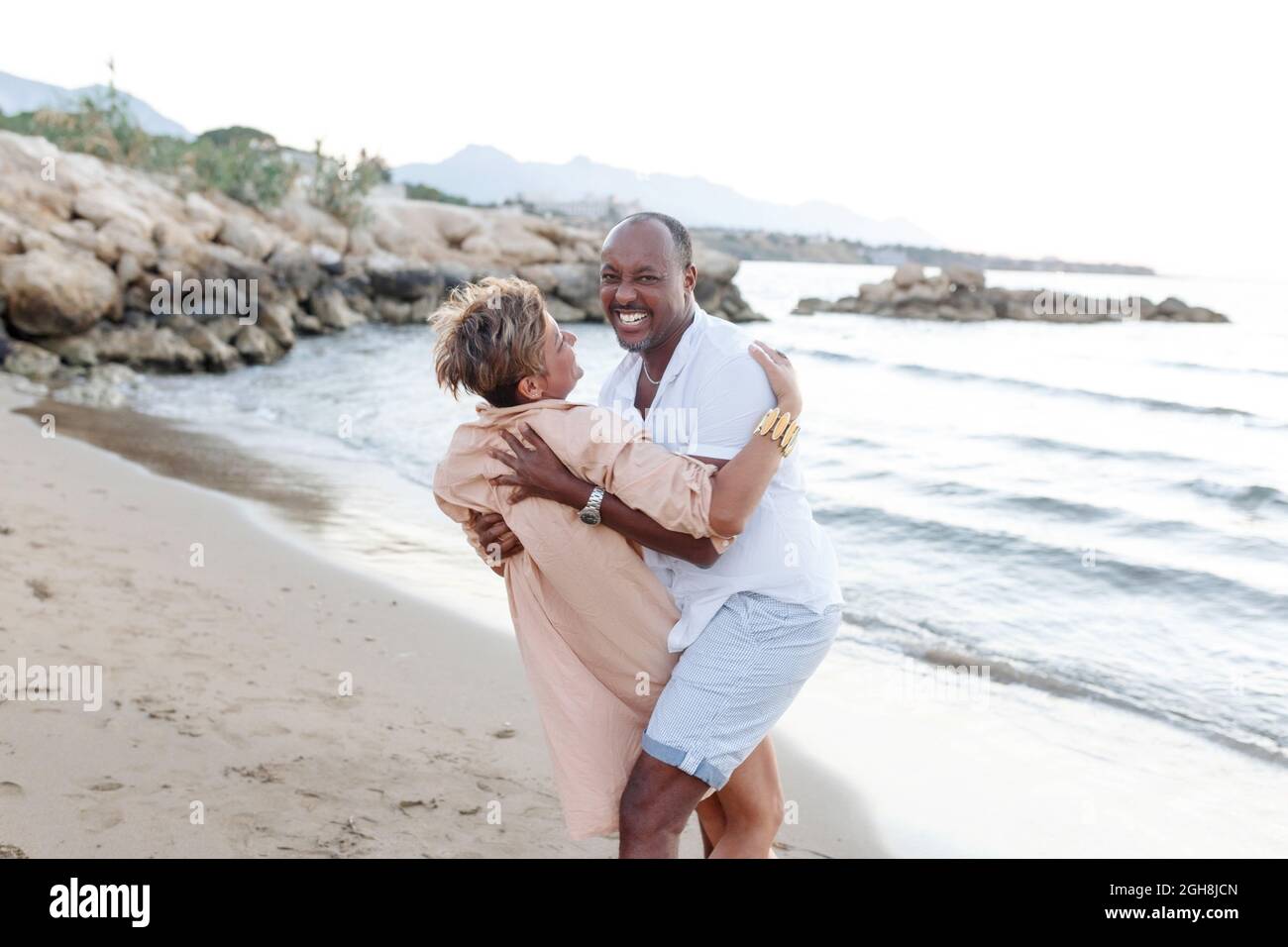 Gara mista sorridente coppia godendo in vacanza, turista che si diverte a piedi sulla spiaggia, diversità e concetto d'amore. Foto Stock