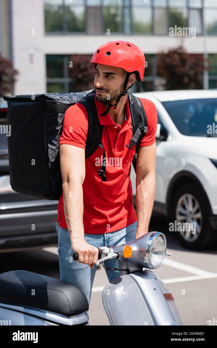 Uomo di liberazione arabo in casco e termo zaino in piedi vicino scooter  all'aperto Foto stock - Alamy