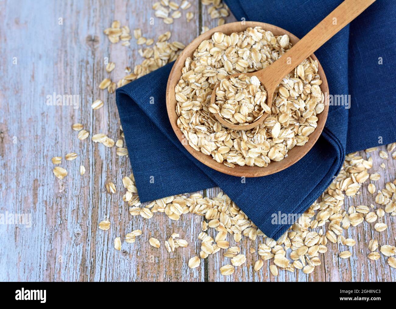 Fiocchi di avena non cotti in ciotola di legno con cucchiaio su tavola rustica. Concetto di alimentazione sana Foto Stock