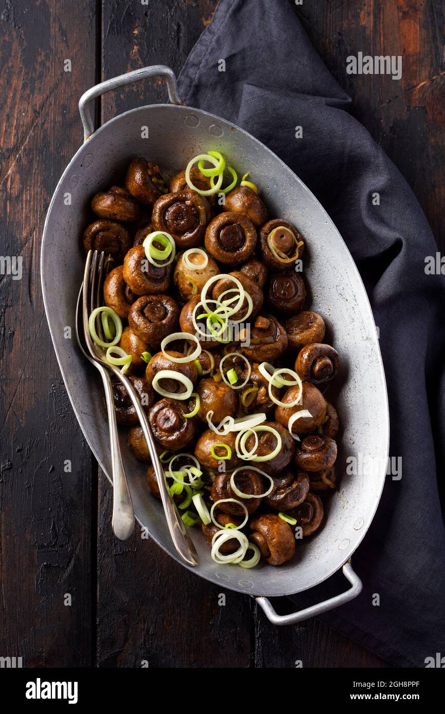 Funghi champignon fritti in salsa di soia, con pepe e cipolle al vapore in una vecchia ciotola di metallo su un vecchio tavolo d'annata. Messa a fuoco selettiva Foto Stock