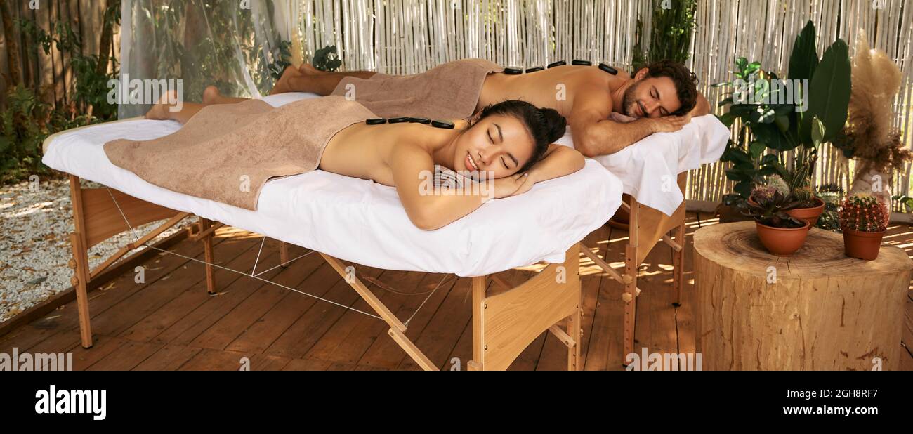 Bella coppia durante il massaggio con pietre calde, giornata congiunta al centro benessere, all'aperto Foto Stock