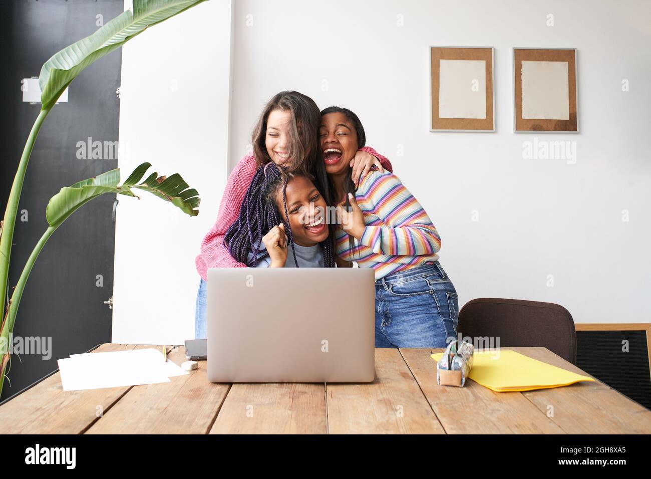 Un gruppo di donne che si abbraccia l'un l'altro festeggia euforicamente le buone notizie davanti al computer. Gruppo multietnico di successo eccitato e felice. Foto Stock