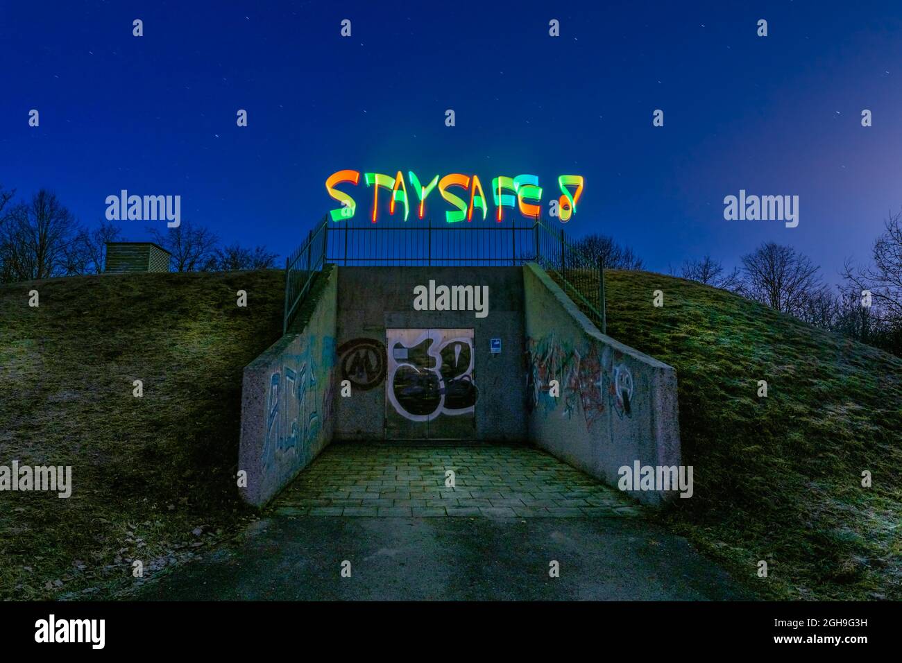I migliori auguri in tempi di Corona e il virus Covid-19, lightpaining di notte con SOGGIORNO SICURO dipinto colorato in cima a un bunker. Foto Stock