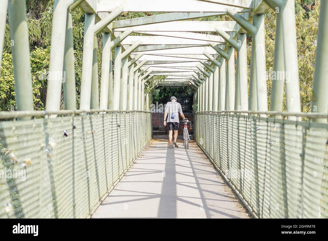Vista posteriore di un ciclista maschio che cammina con la sua bicicletta su un ponte di metallo chiuso Foto Stock