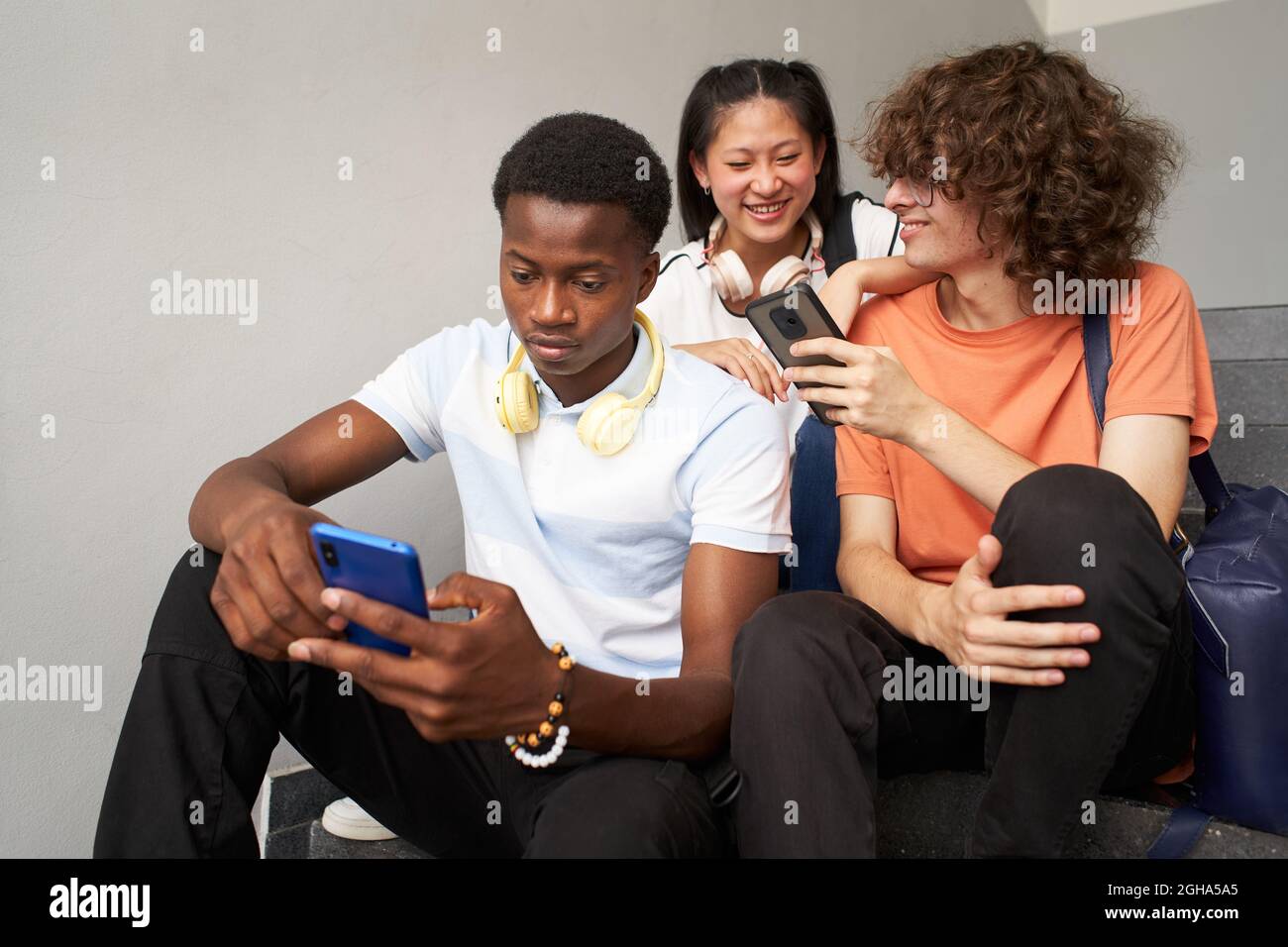 Uno studente afroamericano chiacchiera da solo e i suoi compagni di classe ridono quando usano i loro telefoni cellulari. Foto Stock
