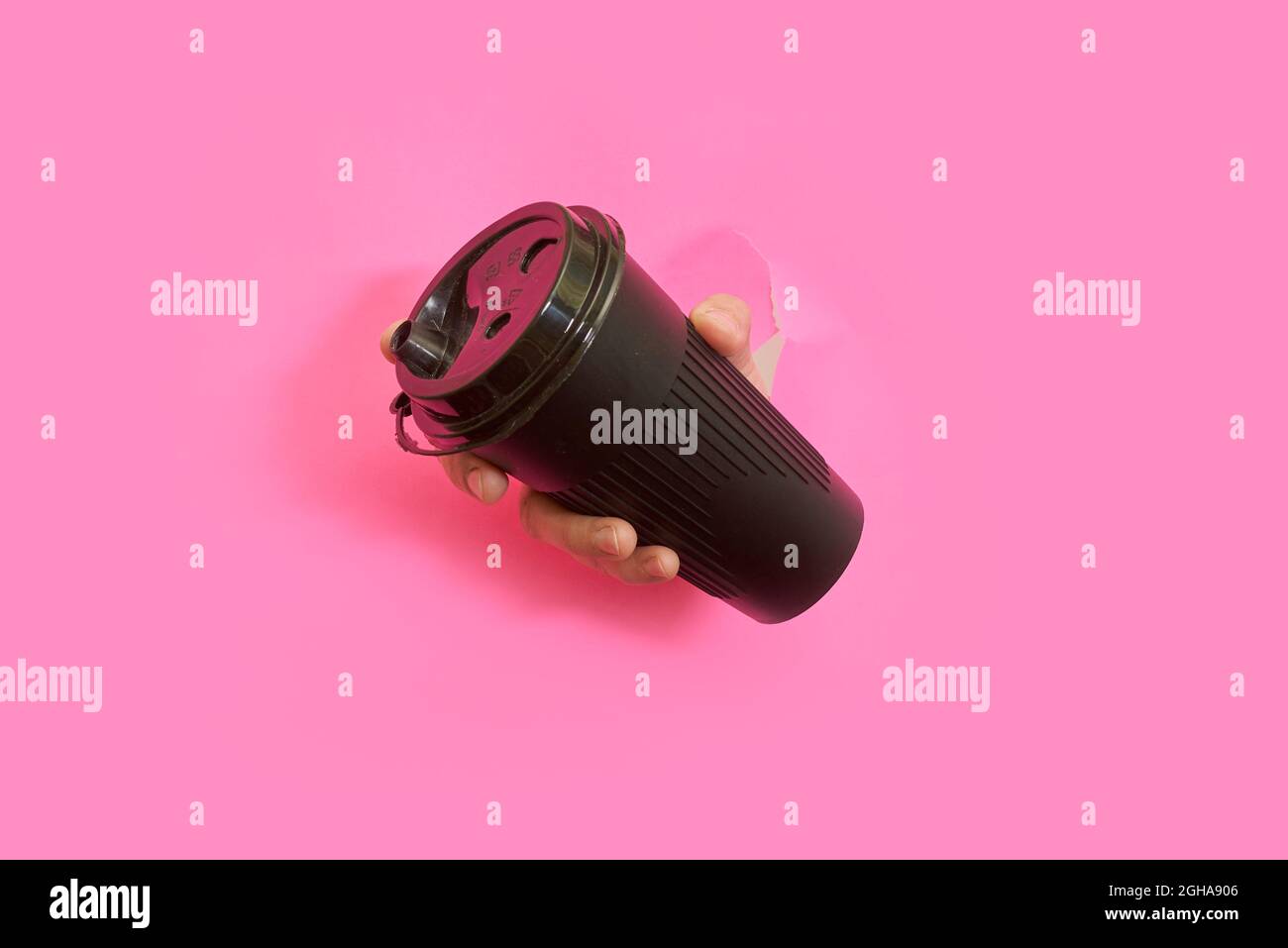Una mano che tiene take away caffè tazza anche se rosa strappato sfondo di carta Foto Stock
