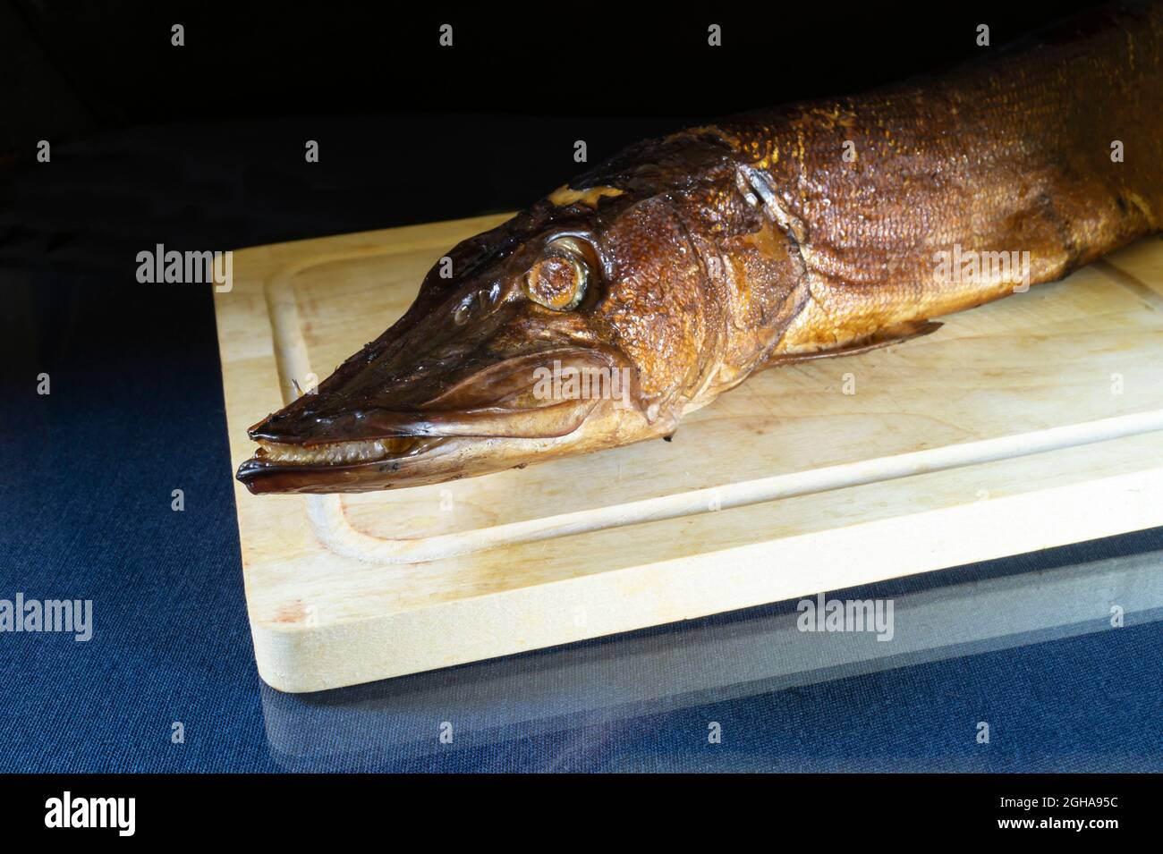 Pike affumicato su un asse di legno con un riflesso. Prodotti alimentari su sfondo nero Foto Stock