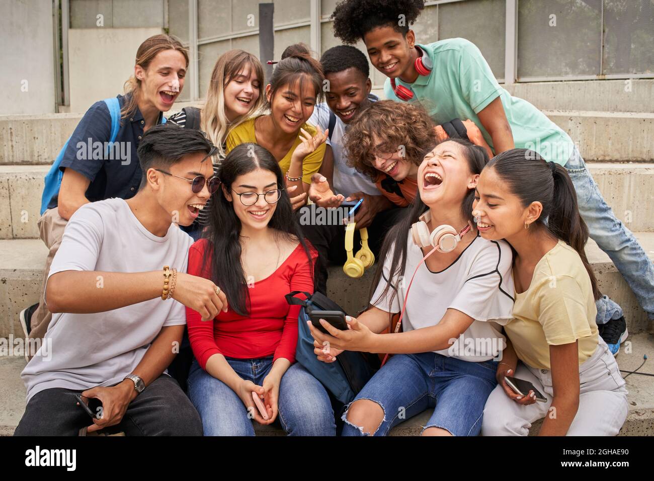 Gruppo multietnico di studenti che usano il cellulare e ridono. Gli adolescenti usano uno smartphone, navigano sul Web. Divertirsi insieme. Foto Stock