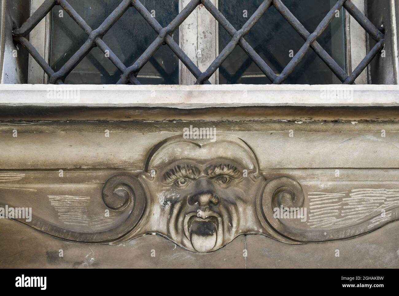 Dettaglio di un antico edificio con bassorilievo che rappresenta il volto accovacciato di un uomo sotto una finestra chiusa da una grata di ferro, Livorno, Toscana, Italia Foto Stock