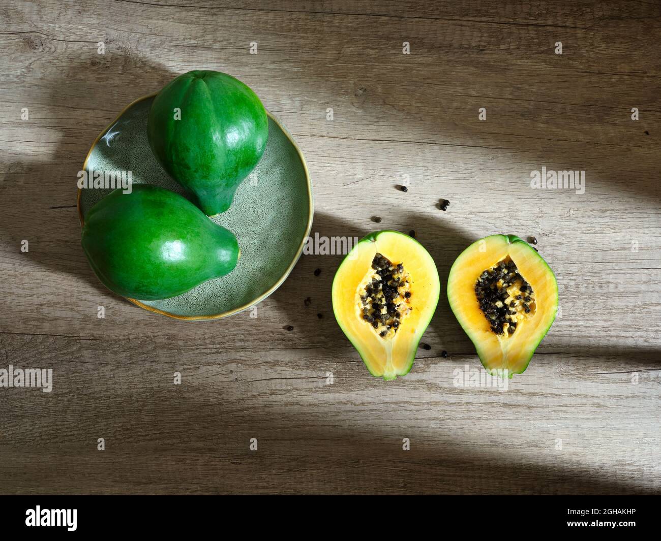 due papaie intere e due metà verdi su superficie di legno Foto Stock