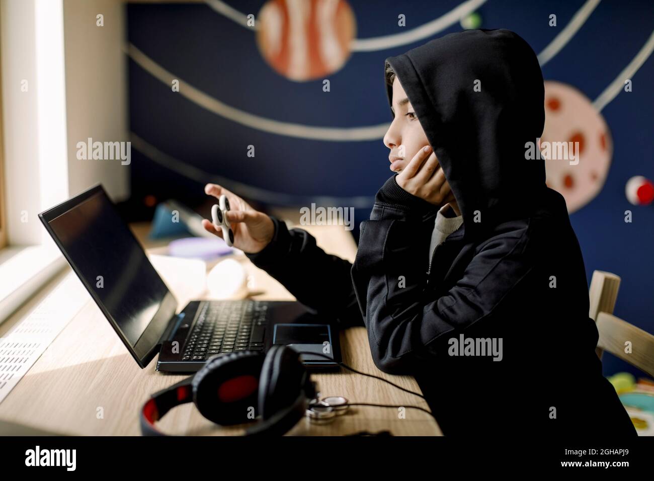 Ragazzo autistico con mano sul mento guardando il computer portatile in camera da letto Foto Stock