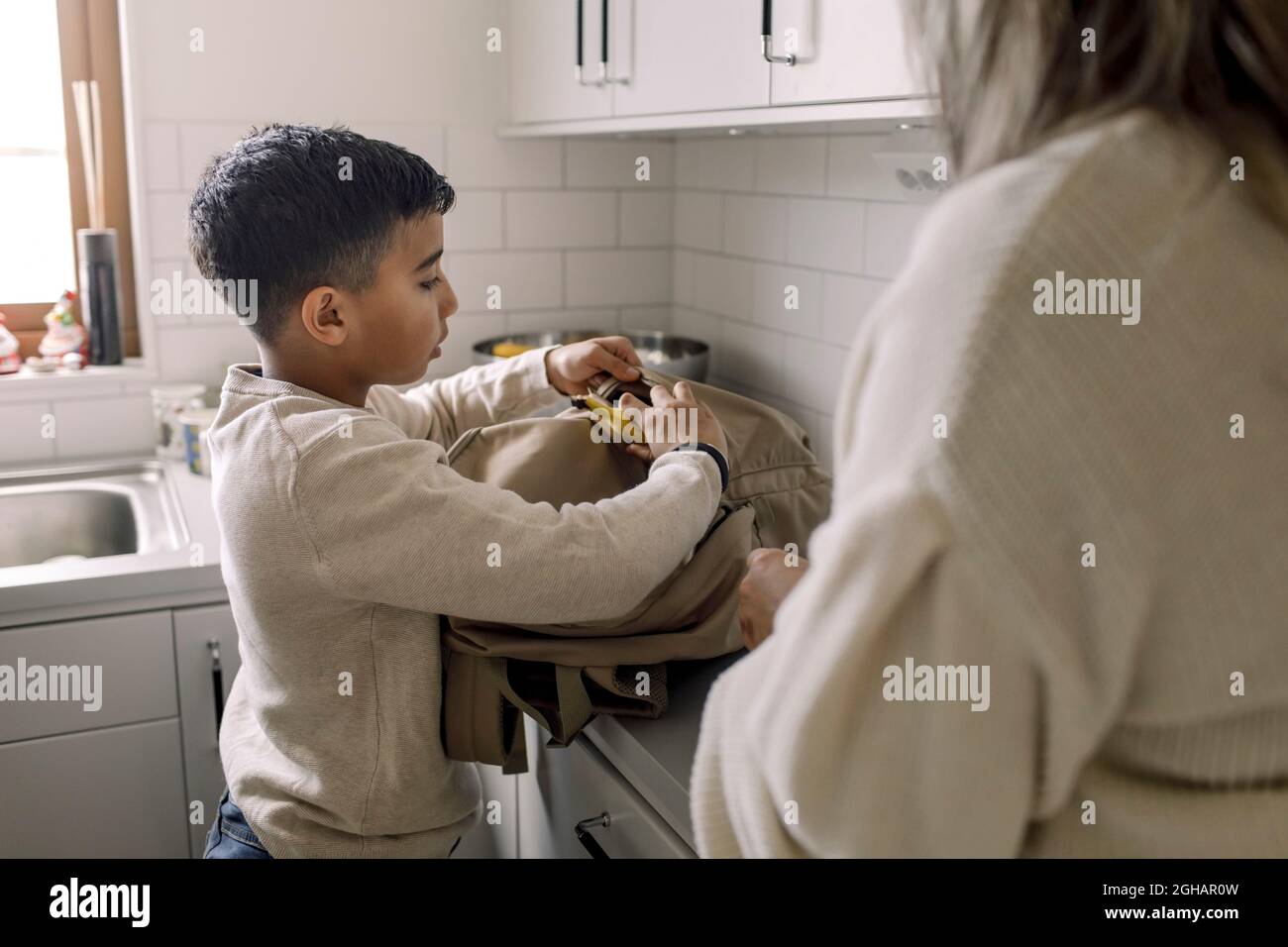 Ragazzo autistico mettere banana in borsa in piedi da madre a casa Foto Stock