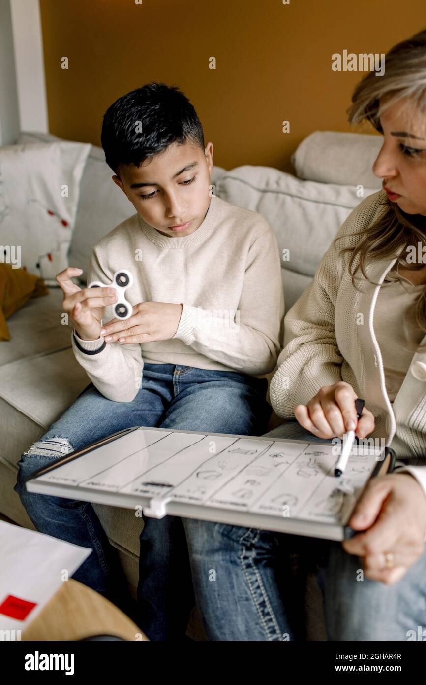 Madre che insegna il ragazzo autistico mentre si siede sul divano nel soggiorno Foto Stock