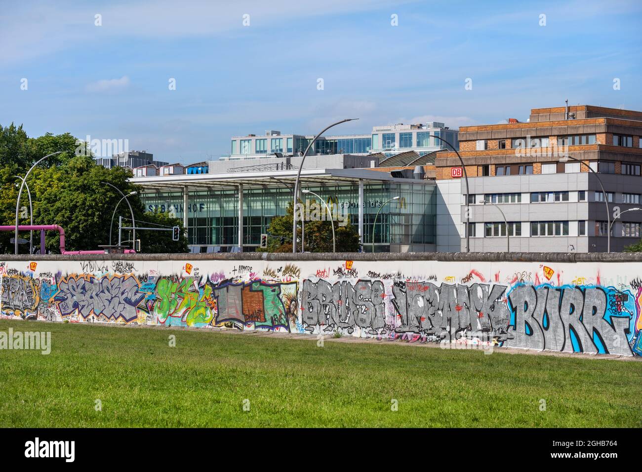 Berlino, Germania - 30 luglio 2021: Muro di Berlino (in tedesco: Berliner Mauer) con ghiaia, lato est, e la stazione ferroviaria di Berlino Ostbahnhof nel backgro Foto Stock