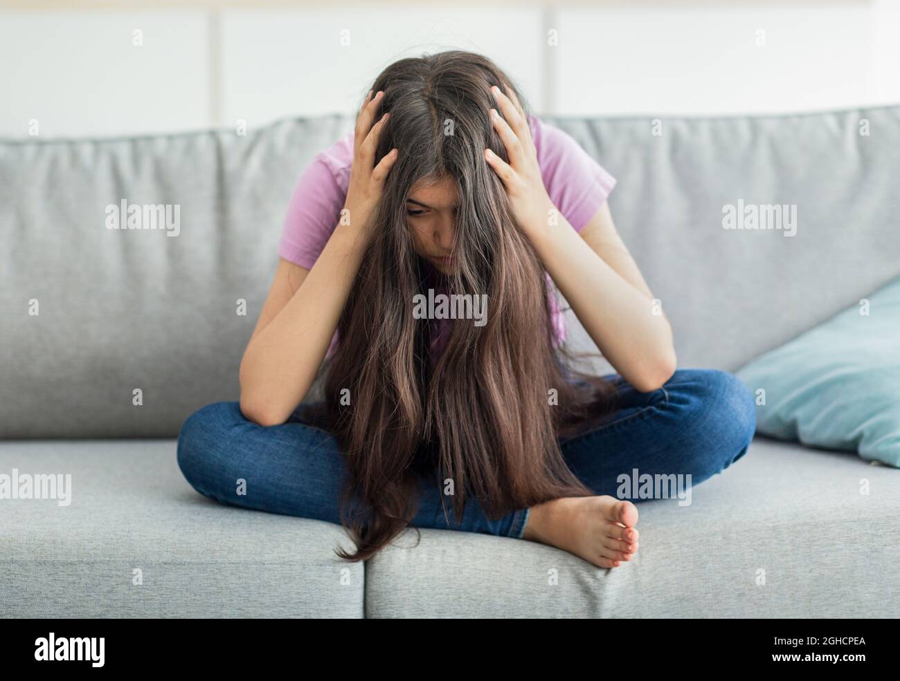 Ragazza indiana teen seduta sul divano testa in mani, assorbita in pensieri negativi, avendo depressione a casa, a tutta lunghezza Foto Stock