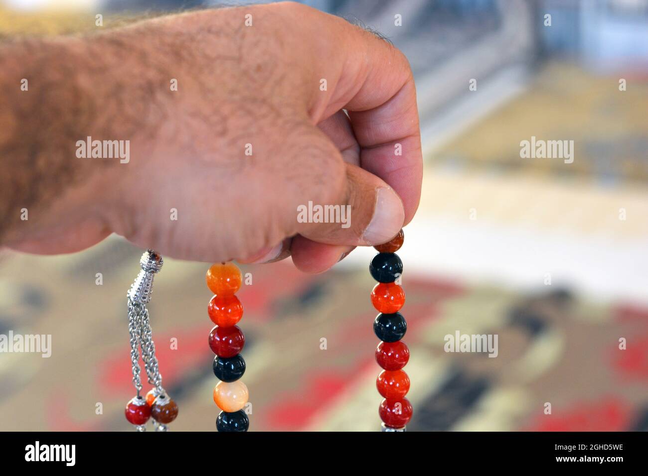 Una mano tiene un rosario islamico colorato su uno sfondo sfocato di un tappeto di preghiera in una moschea, le perle di preghiera islamica chiamato Misbaha o Tasbih, preghiera Foto Stock