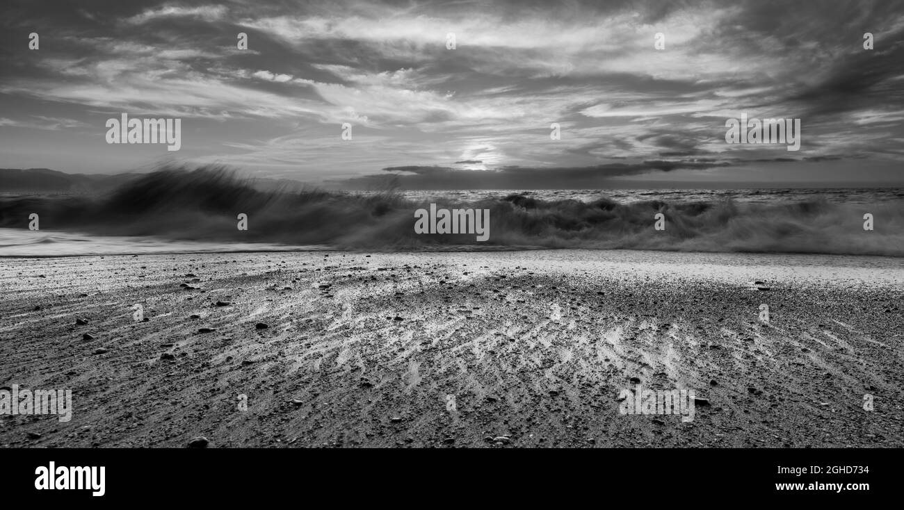 Un bellissimo tramonto sull'oceano con un cielo colorato mentre un'onda si sposta sulla Sandy Shore in formato immagine bianco e nero Foto Stock