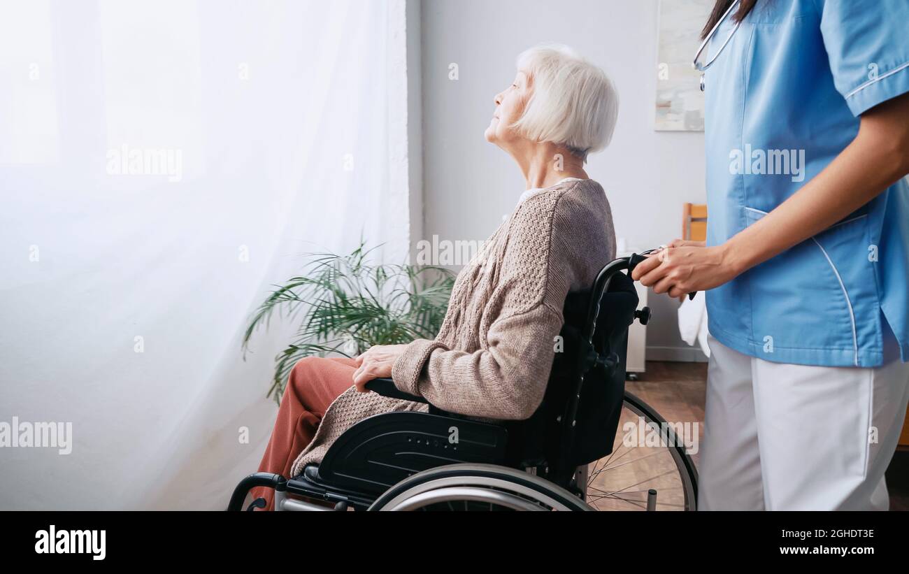 infermiera geriatrica che sposta una donna anziana in sedia a rotelle Foto Stock