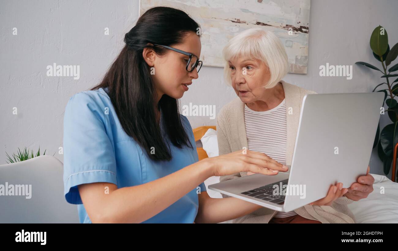 infermiere geriatrico brunette che mostra alle donne anziane come usare il laptop Foto Stock