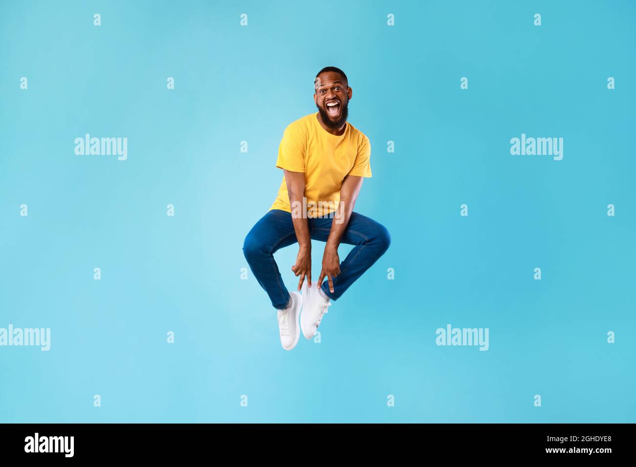 Pazzo africano americano ragazzo saltare in su e fare gesto di pace con entrambe le mani su sfondo blu studio Foto Stock