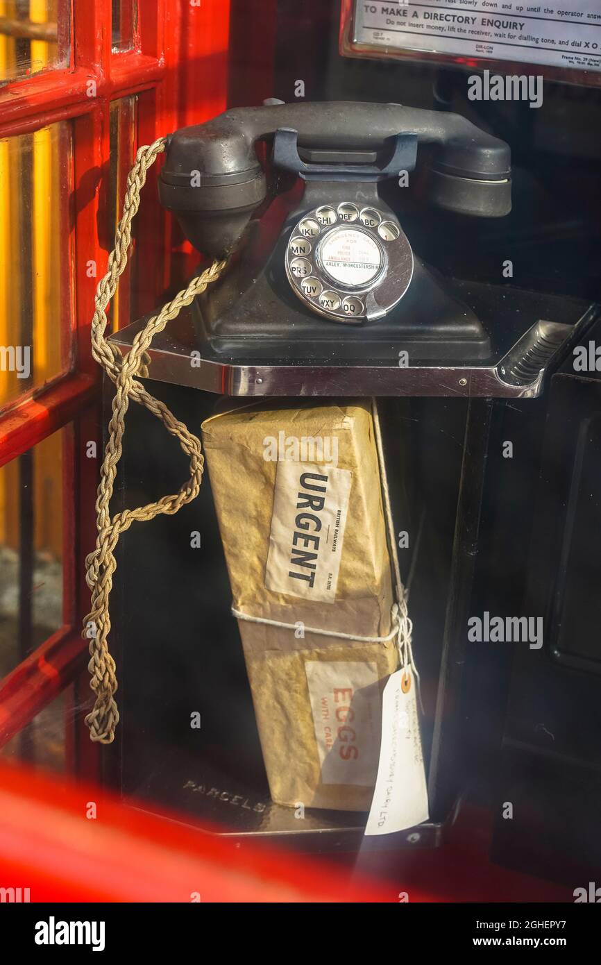 Guarda attraverso il vetro di un vecchio e tradizionale telefono rosso britannico che guarda un pacco urgente lasciato sul ripiano sotto il microtelefono vintage. Foto Stock