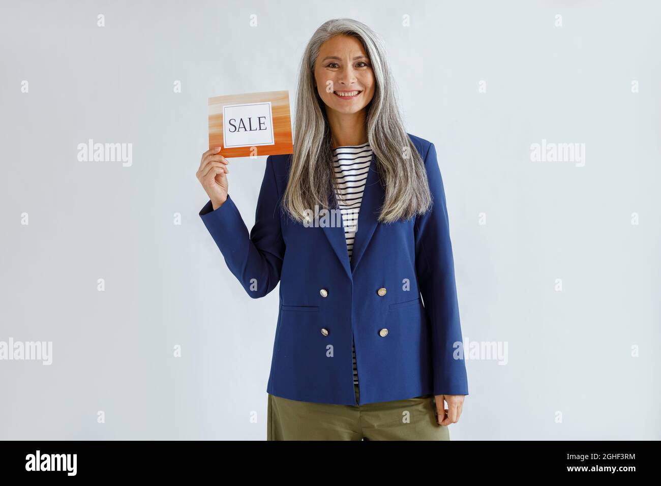 Graziosa signora asiatica con capelli grigi tiene la carta con parola sale su sfondo chiaro Foto Stock