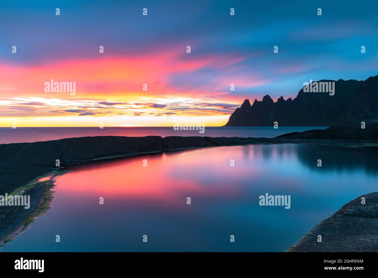 Lunga esposizione del mare colorato da calde luci di mezzanotte sole dal punto di vista di Tungeneset, Senja, contea di Troms, Norvegia Foto Stock