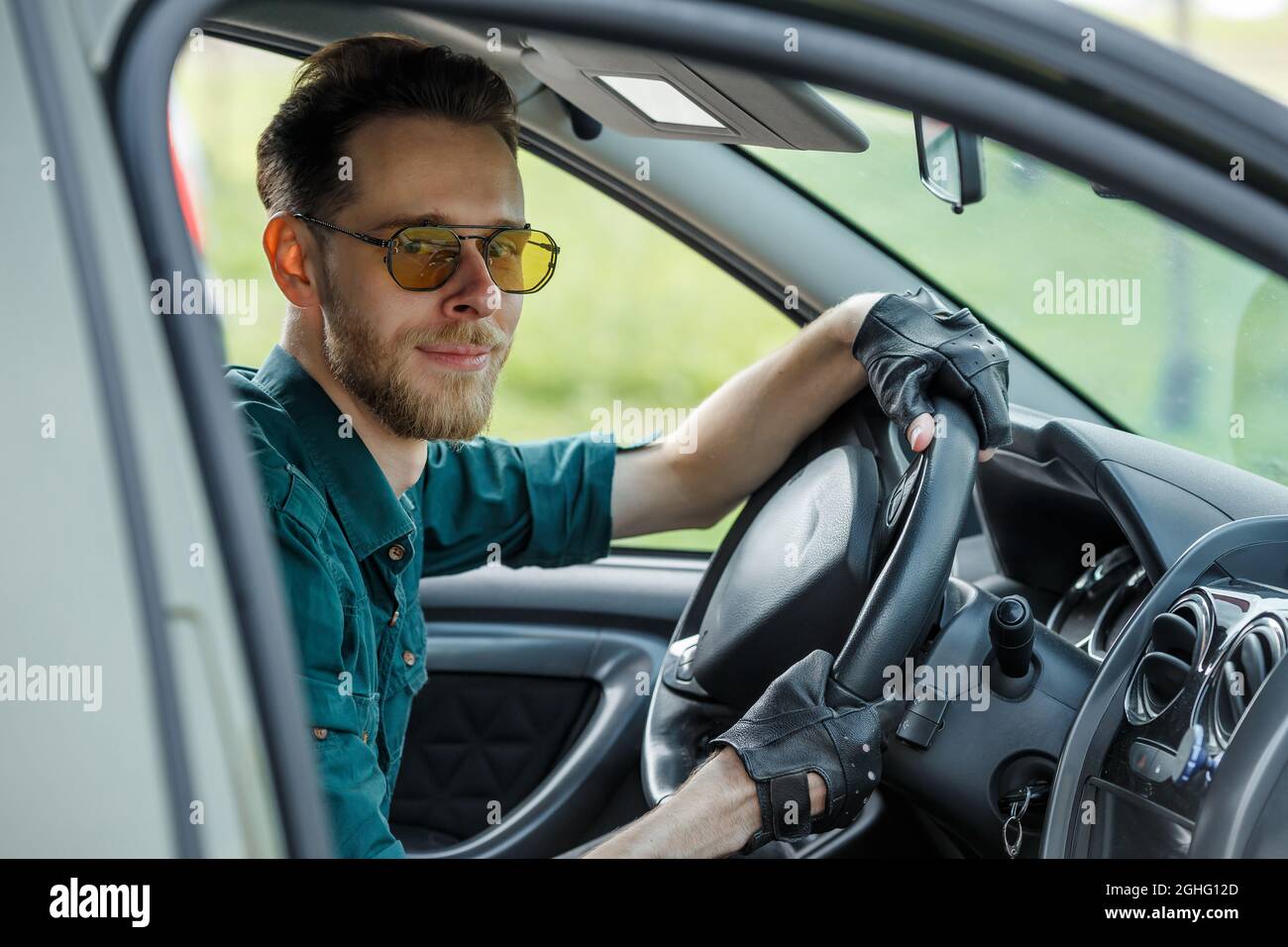 Ritratto di un giovane uomo in occhiali scuri guida una macchina e sorridente Foto Stock