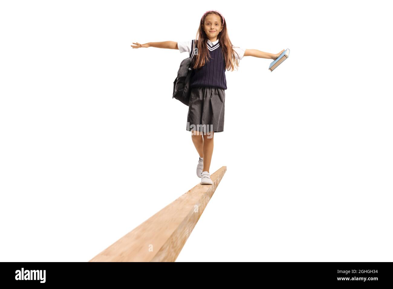 Studentessa in uniforme che porta uno zaino e cammina su un fascio di legno isolato su sfondo bianco Foto Stock