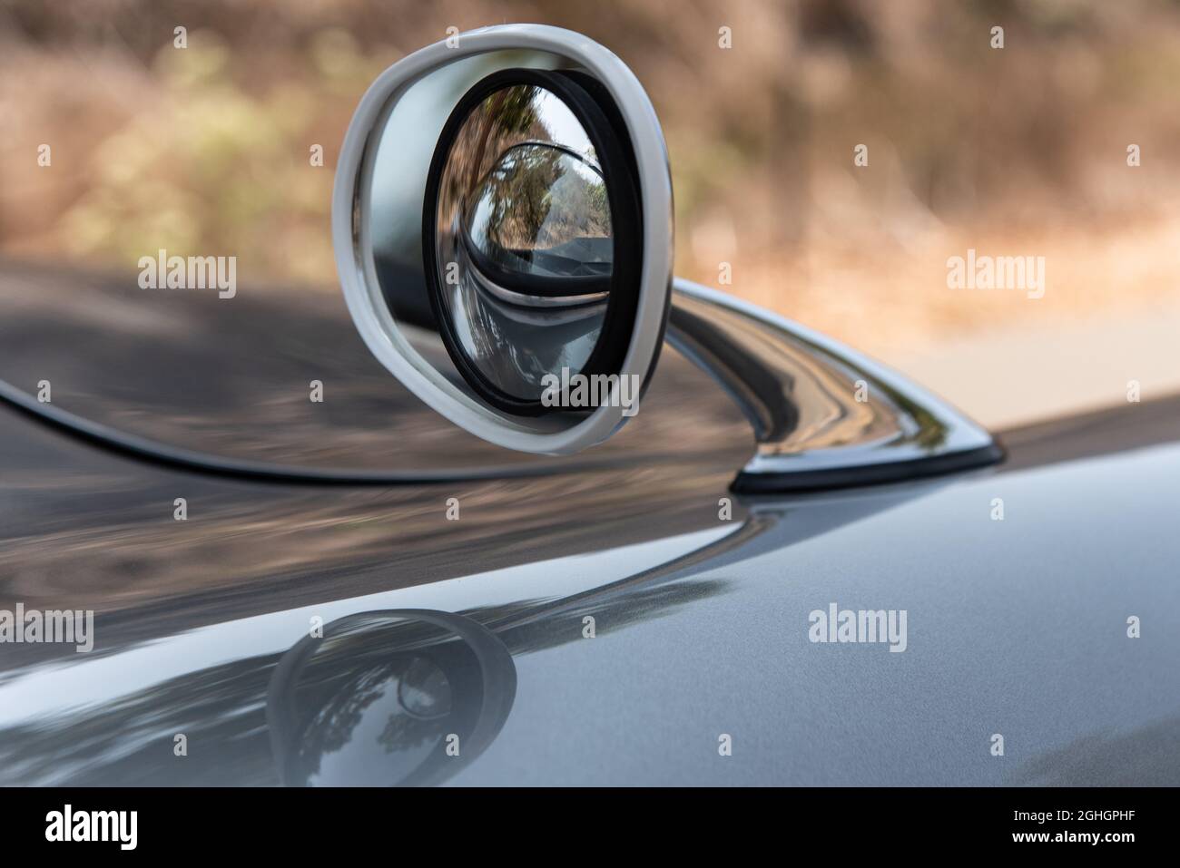 Lo specchio retrovisore cromato lucido con obiettivo grandangolare convesso e gonfio di un'auto sportiva senza tempo ha linee lunghe e curvilinee. Foto Stock